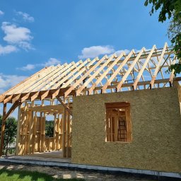 ENERGO DOM SPÓŁKA Z OGRANICZONĄ ODPOWIEDZIALNOŚCIĄ - Konstrukcja domu szkieletowego w trakcie budowy, widoczna więźba dachowa i ściany z płyt OSB, błękitne niebo w tle. Ujęcie z poziomu gruntu.