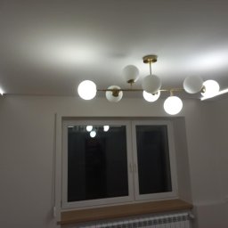 Gładzie Nowacki - Nowoczesne oświetlenie sufitowe z ledami wzdłuż krawędzi sufitu i lampą kulistą. Świeżo pomalowane ściany w neutralnym odcieniu. Widok na okno.