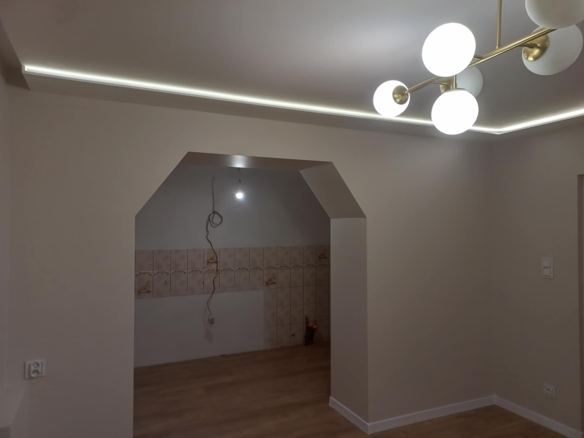 Jasne wnętrze po remoncie z oświetleniem LED w suficie i nowoczesną lampą. Widoczne gładkie ściany i wykończone przejście między pomieszczeniami.