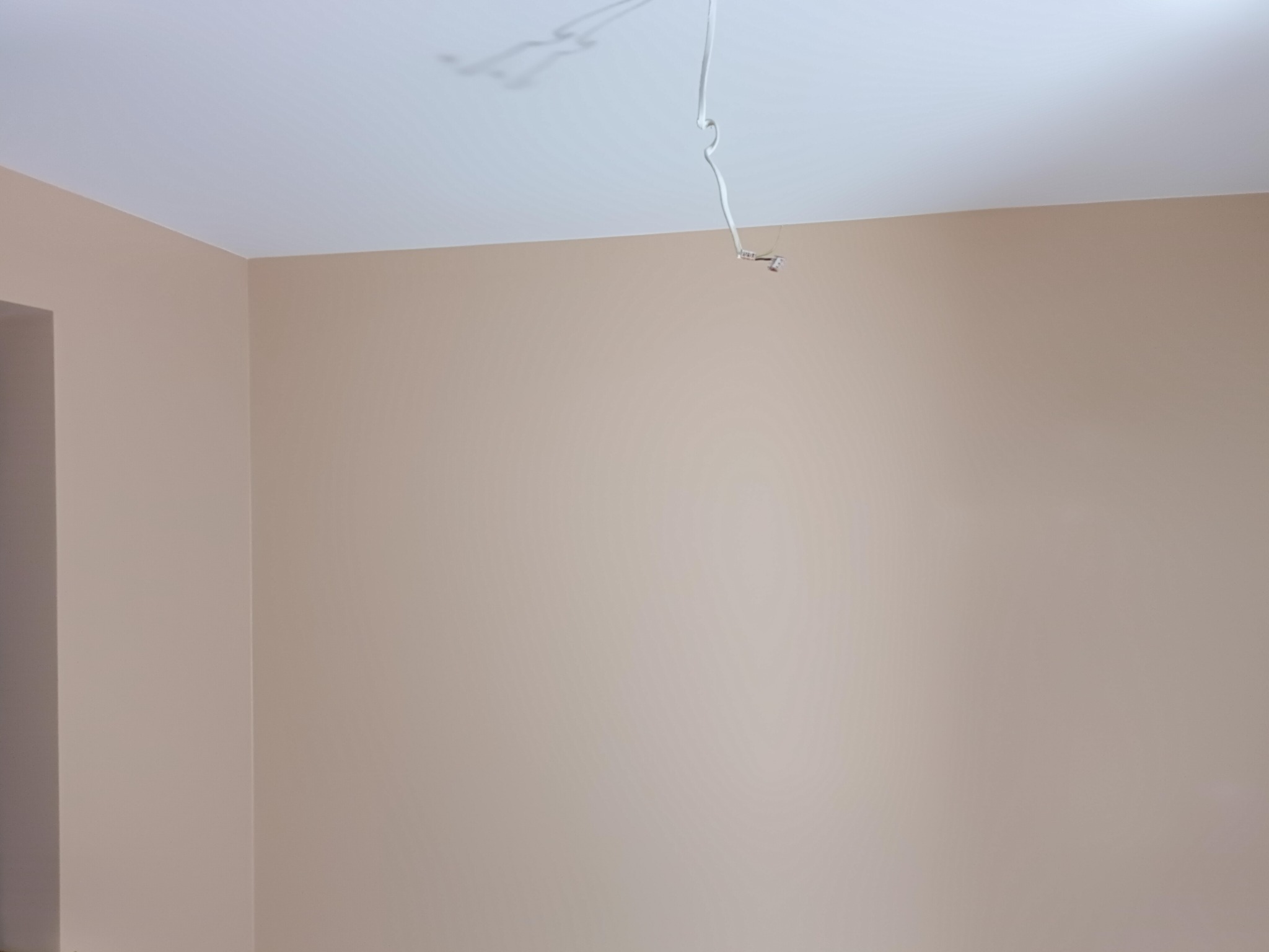 Świeżo pomalowane ściany w odcieniach beżu w pustym pokoju, widoczne przewody elektryczne zwisające z sufitu, gotowe do montażu oświetlenia.