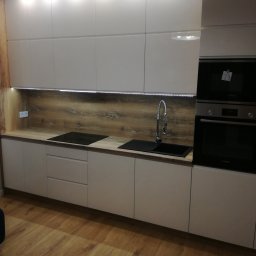 Usługi budowlane Piotr Skraburski - Nowoczesna kuchnia z białymi szafkami, drewnianym blatem i oświetleniem LED. Widoczny zlew, płyta indukcyjna i piekarnik. Parkiet na podłodze.