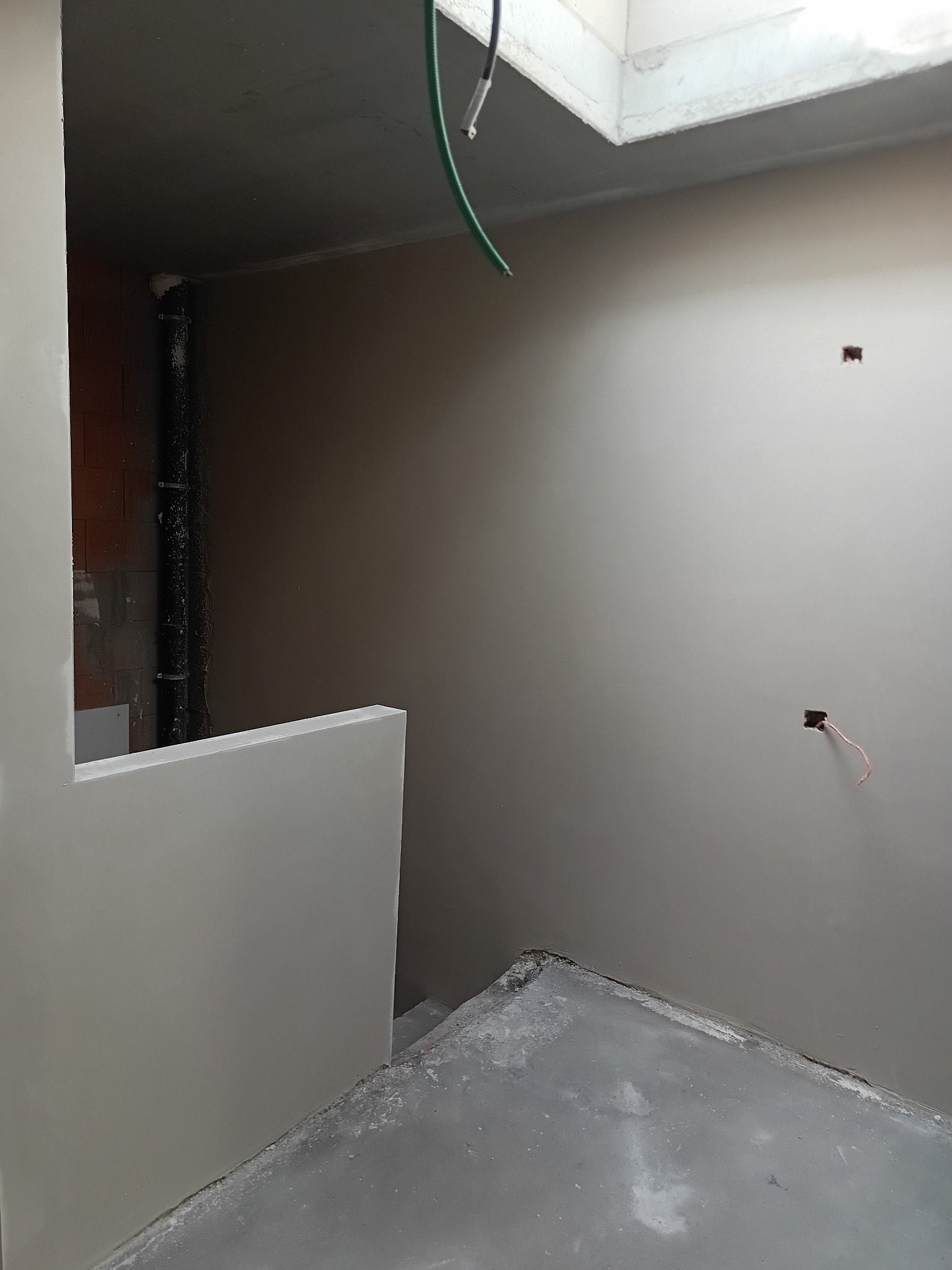 Wnętrze po szpachlowaniu ścian i sufitu, widoczne gładkie powierzchnie przygotowane do malowania. Otwór okienny w suficie doświetla pomieszczenie. Fragment instalacji elektrycznej.