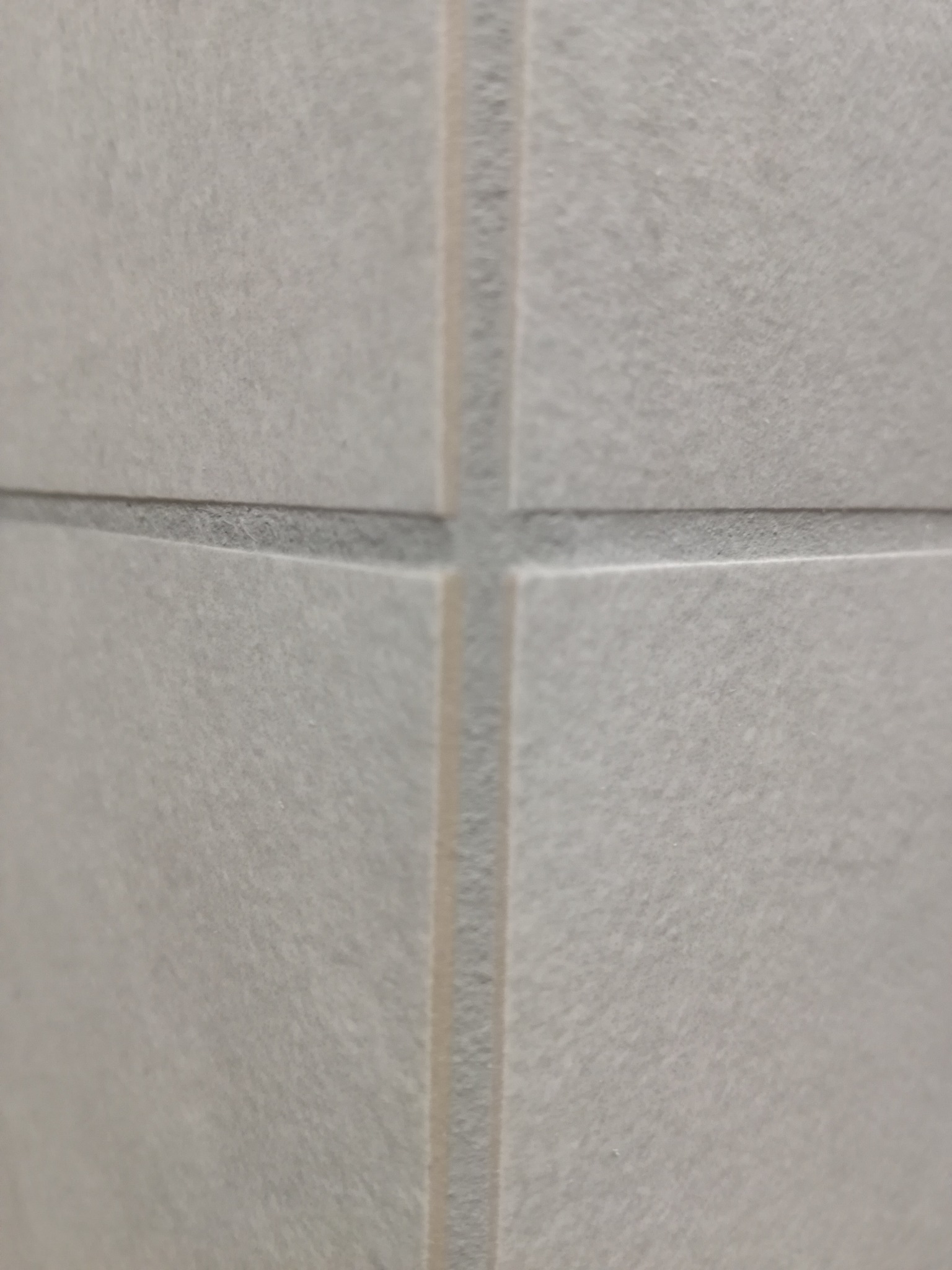 Zbliżenie na jasnoszare, matowe płytki ceramiczne ułożone w regularną siatkę z szarymi fugami. Widoczna faktura płytek i precyzja wykonania spoin.