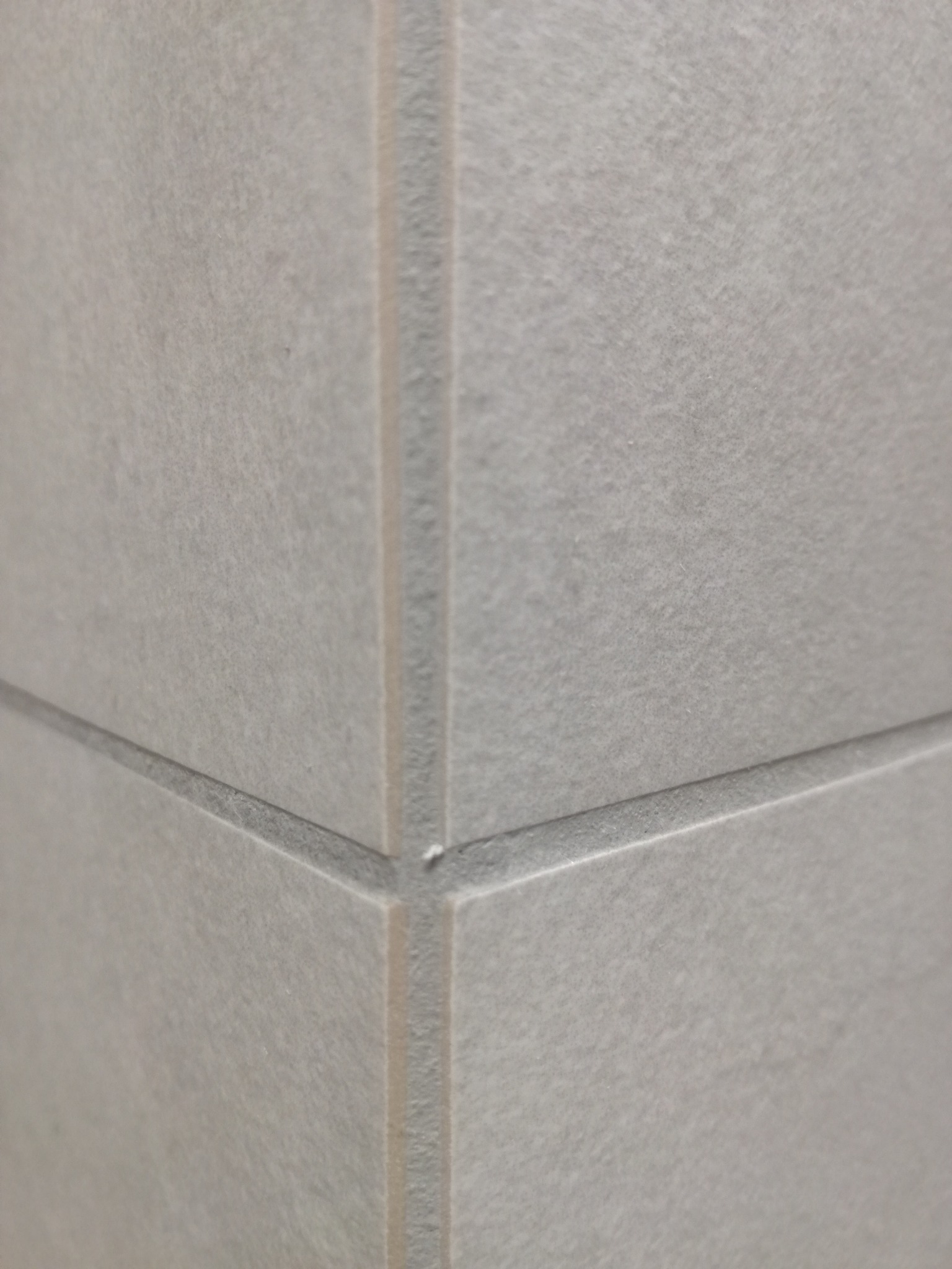 Szczegółowe ujęcie narożnika wykończonego jasnoszarą, matową płytką ceramiczną z wyraźnie zaznaczoną fugą. Minimalistyczny design, neutralna kolorystyka.
