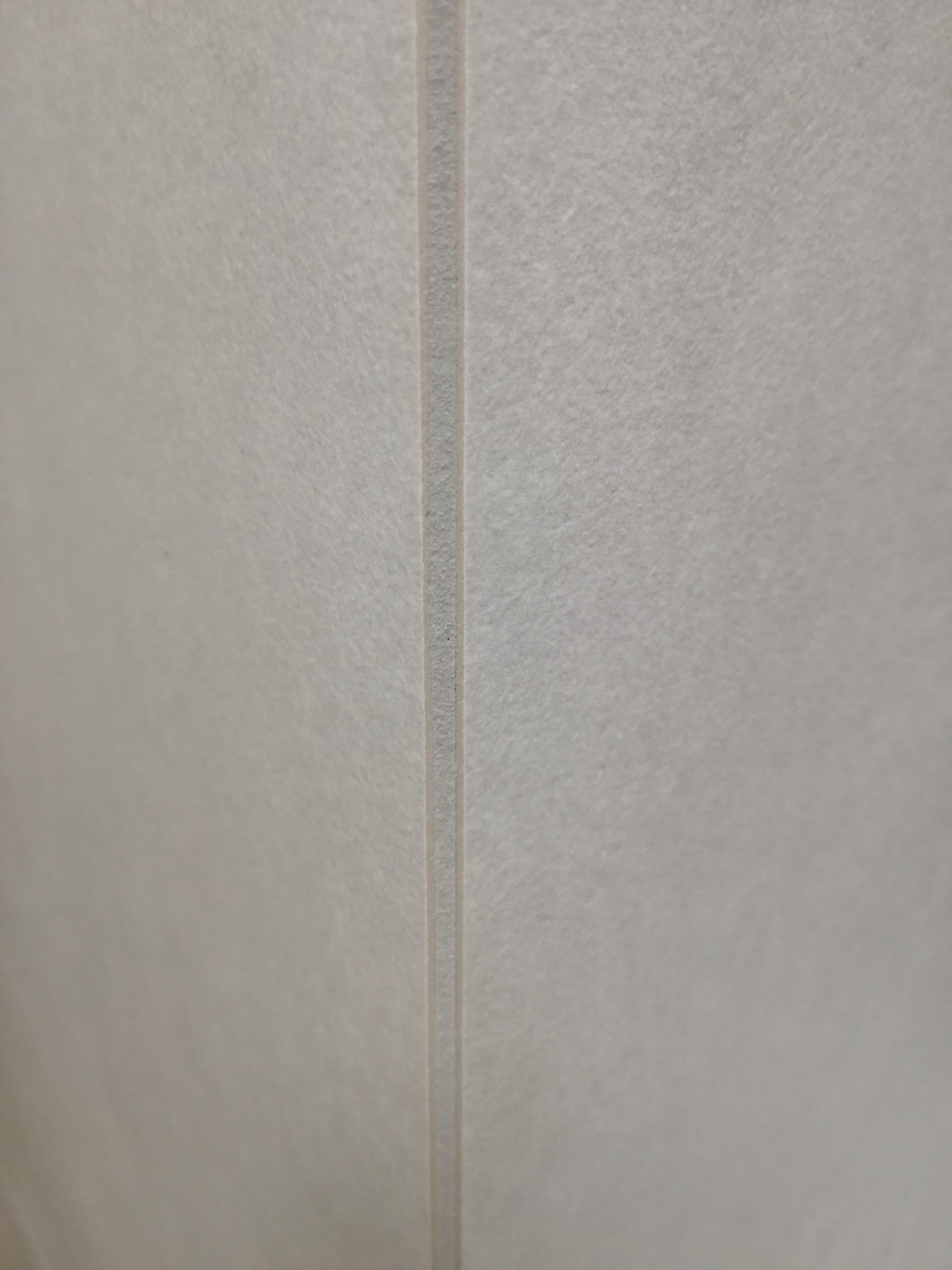 Jasnoszara, matowa powierzchnia z delikatną fakturą i pionową fugą. Minimalistyczny detal wykończenia ściany lub podłogi, bliski kadr.