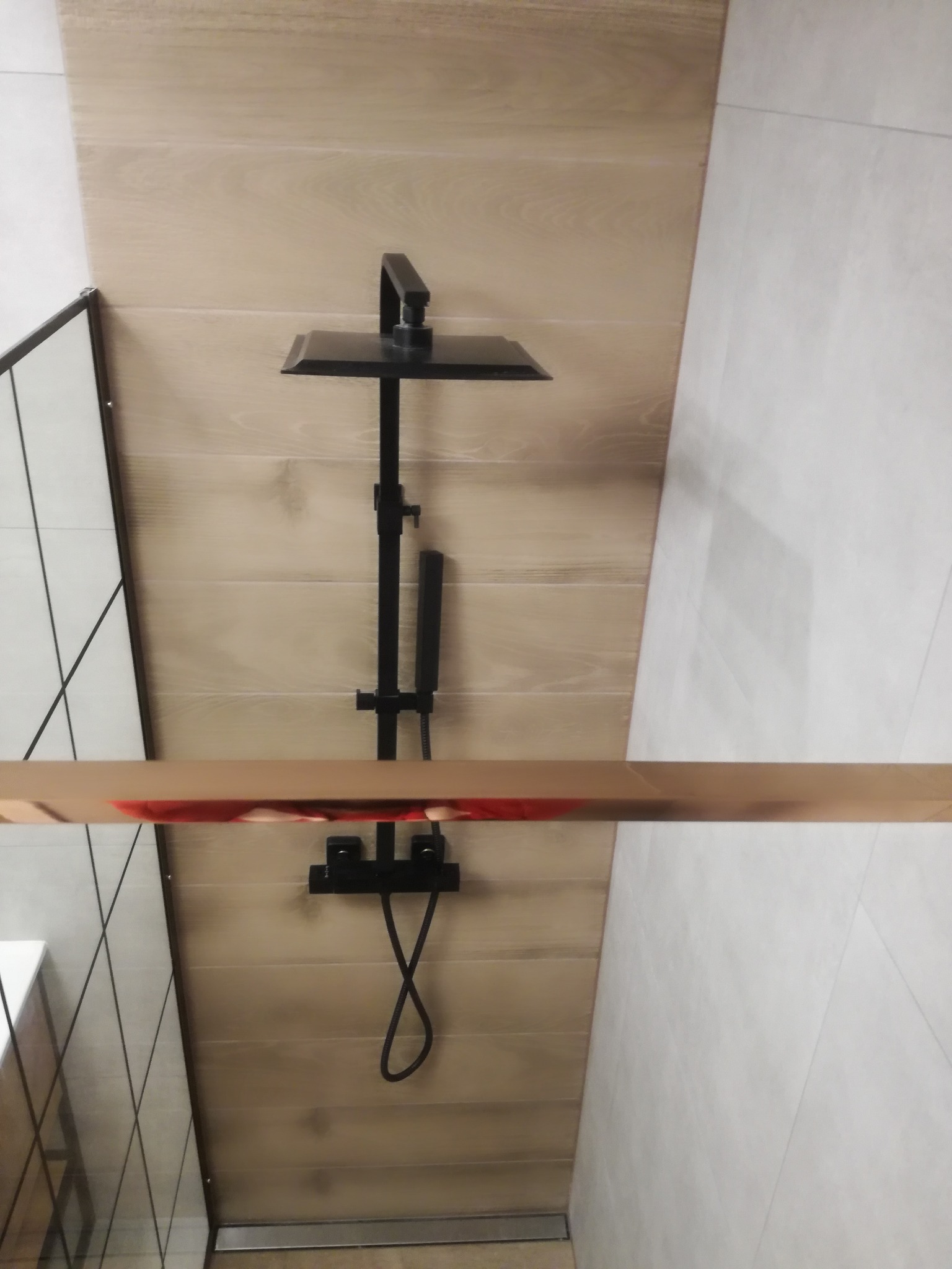 Nowoczesna kabina prysznicowa z czarną armaturą i panelami imitującymi drewno. Minimalistyczny design, jasne płytki, widok z góry.