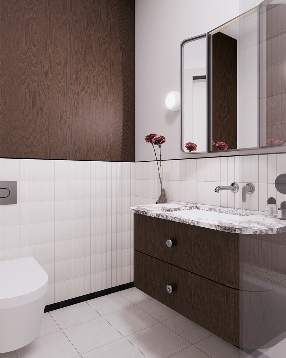 Nowoczesna łazienka z drewnianymi szafkami, białymi płytkami i marmurowym blatem umywalki. Minimalistyczny design z kwiatami w wazonie i okrągłym lustrem.