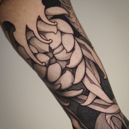 Amber Tattoo Wrocław - Czarno-biały tatuaż na ramieniu z motywem kwiatowym i elementami abstrakcyjnymi, wykonany z dbałością o detale i cieniowanie, widoczne logo wykonawcy w rogu.