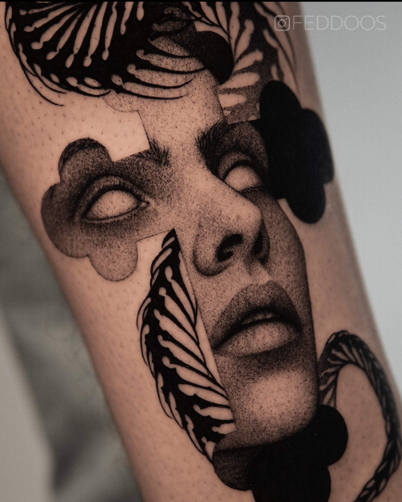 Czarno-biały tatuaż na ramieniu przedstawiający twarz kobiety z abstrakcyjnymi elementami roślinnymi. Wyraźny kontrast, artystyczny styl, widoczne detale skóry.