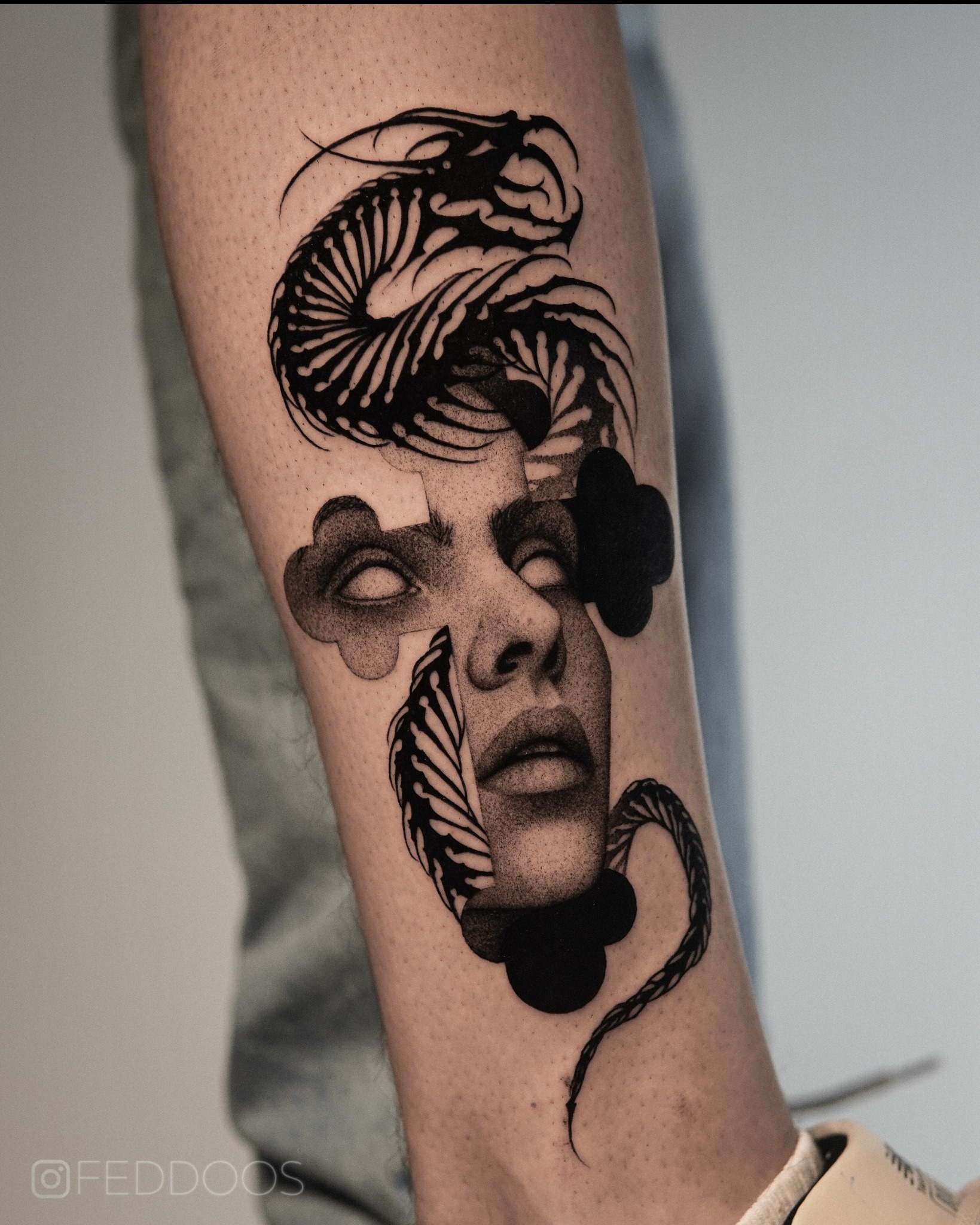 Czarno-biały tatuaż na przedramieniu przedstawiający twarz kobiety z elementami roślinnymi i abstrakcyjnymi, wykonany w technice dotwork.