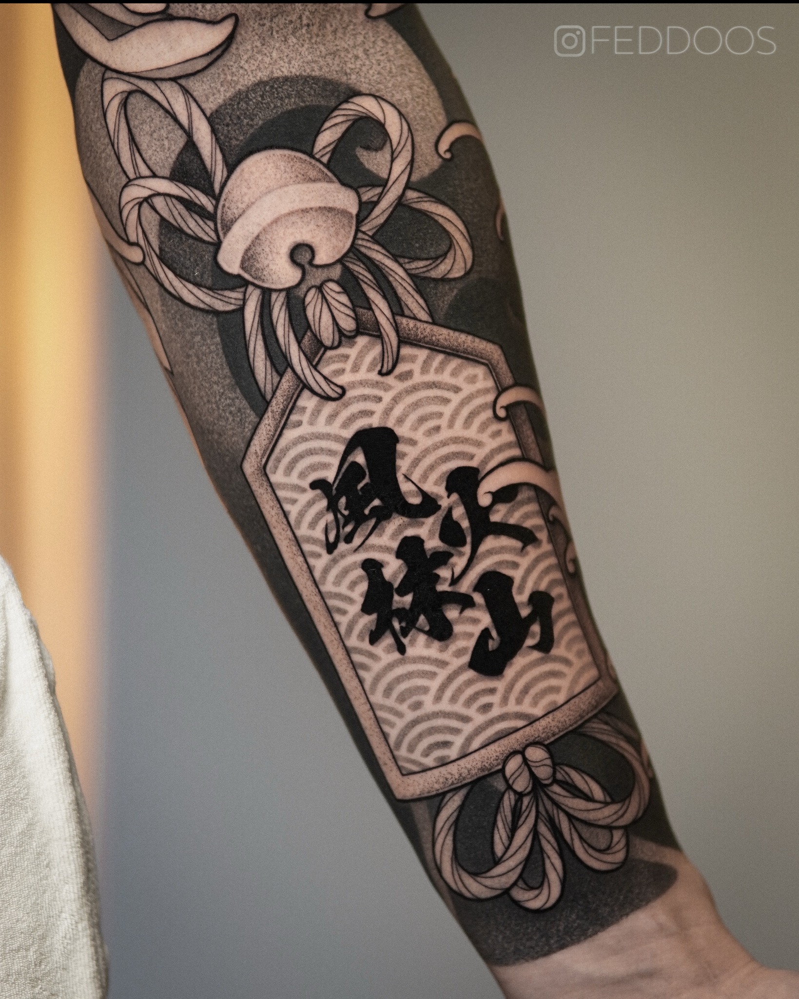 Ramię z unikalnym tatuażem w stylu japońskim, wykonanym we Wrocławiu. Czarno-biały wzór z motywem fal i znaków, precyzyjne cieniowanie, widoczny efekt końcowy.