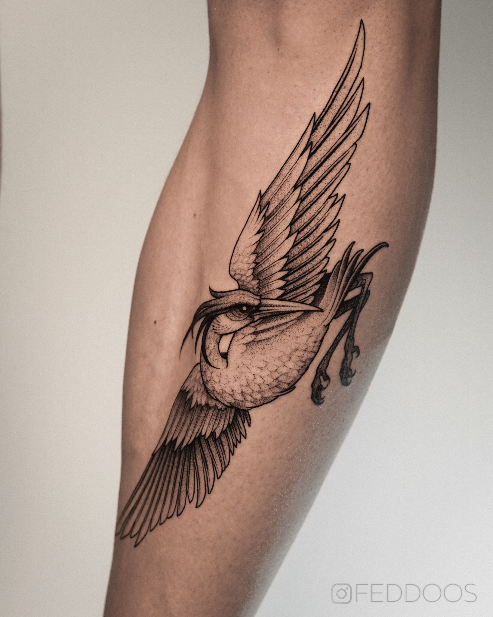 Czarno-biały tatuaż przedstawiający stylizowanego żurawia w locie, umieszczony na łydce. Delikatne cieniowanie i precyzyjne linie tworzą unikalny wzór.