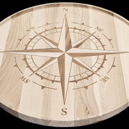 WOOD METAL ART SPÓŁKA Z OGRANICZONĄ ODPOWIEDZIALNOŚCIĄ - Okrągły, drewniany blat z wygrawerowaną różą kompasową. Jasne drewno z wyraźnym usłojeniem. Precyzyjne detale grawerunku. Widoczne oznaczenia kierunków świata.