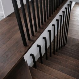 WOOD METAL ART SPÓŁKA Z OGRANICZONĄ ODPOWIEDZIALNOŚCIĄ - Nowoczesne schody z ciemnego drewna z czarnymi, minimalistycznymi balustradami. Widok z góry, ukazujący detale wykończenia i kontrast materiałów.