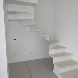 WOOD METAL ART SPÓŁKA Z OGRANICZONĄ ODPOWIEDZIALNOŚCIĄ - Minimalistyczne, białe schody w jasnym wnętrzu. Stopnie wspornikowe, bez balustrady, z widocznymi mocowaniami. Podłoga zabezpieczona folią ochronną.