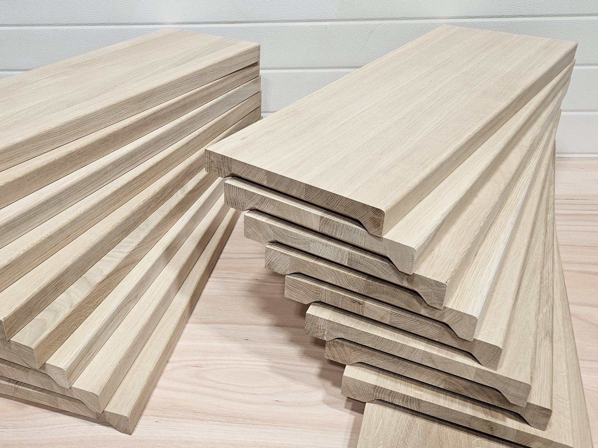 Stos jasnych, drewnianych stopni schodowych z frezowanymi krawędziami, ułożonych na blacie. Widoczna struktura drewna i precyzyjne wykończenie elementów.