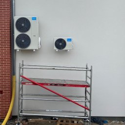 CoolPro Bogumił Brzozowski - Dwa klimatyzatory Midea zamontowane na białej ścianie budynku z ceglanymi elementami dekoracyjnymi. Widoczne rusztowanie.