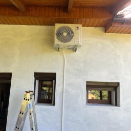 CoolPro Bogumił Brzozowski - Zamontowana jednostka zewnętrzna klimatyzacji marki Gree na elewacji budynku z widoczną drabinką i dwoma oknami z brązowymi ramami.