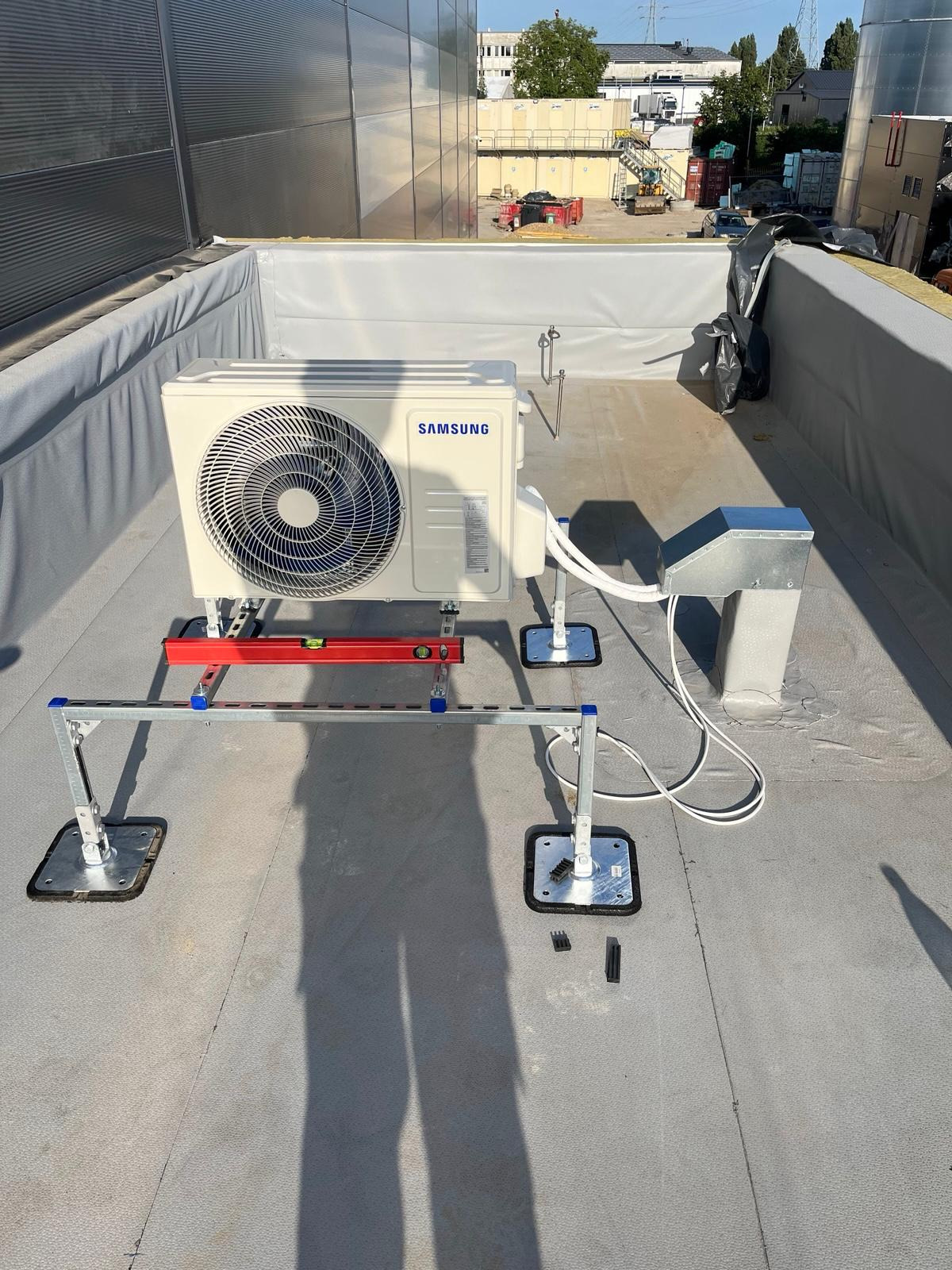 Klimatyzator Samsung zamontowany na dachu budynku, widoczne elementy montażowe i przewody. Instalacja na płaskim dachu z użyciem specjalnej konstrukcji wsporczej.