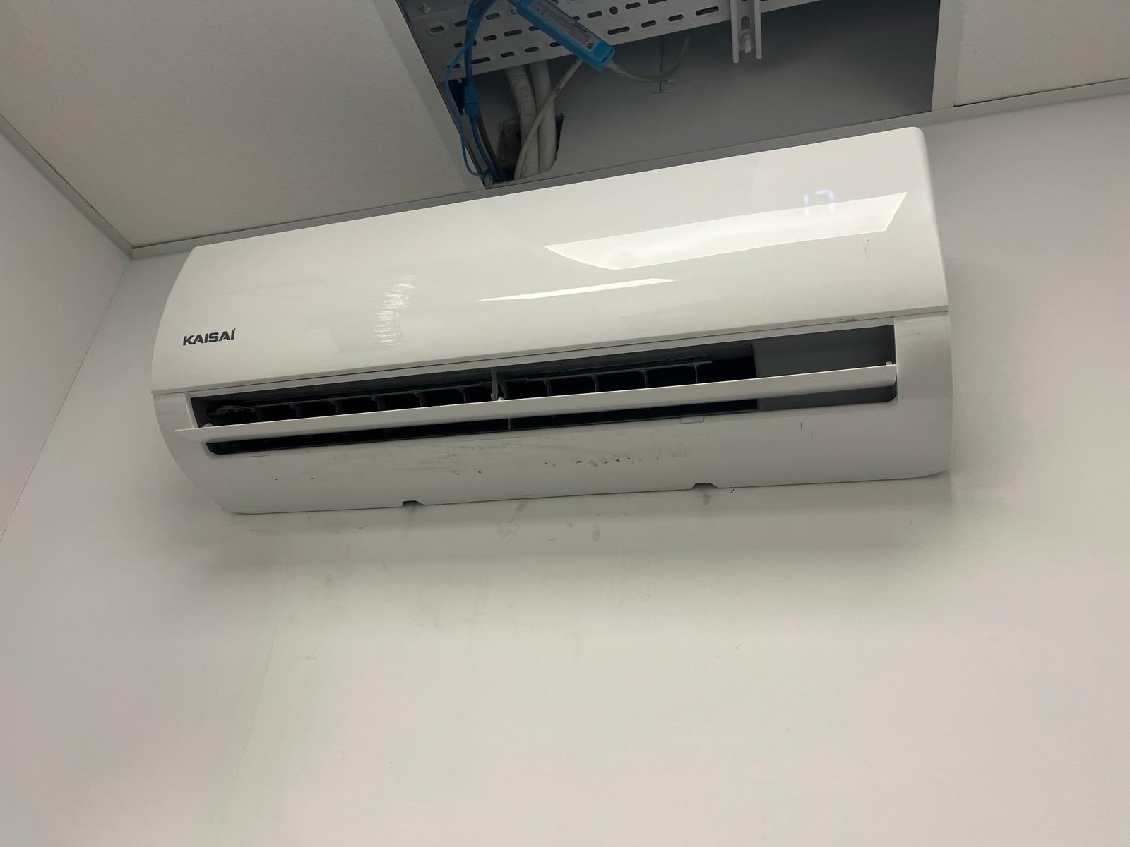 Biała klimatyzacja Kaisai zamontowana na białej ścianie, widoczne przewody w suficie podwieszanym. Na wyświetlaczu urządzenia widoczna temperatura 17 stopni.