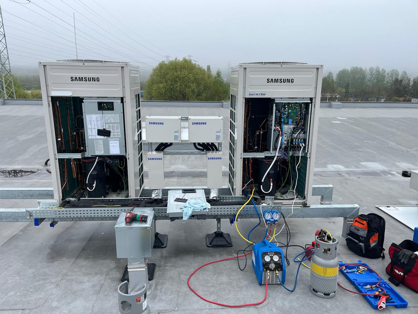 Instalacja klimatyzacji Samsung na dachu budynku. Widoczne narzędzia serwisowe i elementy instalacji. Prace w toku, otwarte obudowy jednostek zewnętrznych.