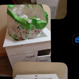 Kacper Pilecki - Opróżniona szafka łazienkowa z umywalką, obok torba z odpadami i elementy demontażu. Widoczne ślady użytkowania i demontażu.