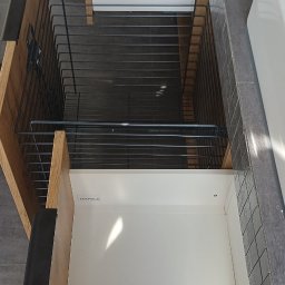 JSM Meble Jarosław Składaniec - Otwarta szafka łazienkowa z drewnianymi frontami i metalowym koszem na akcesoria, widok z góry, z widocznym logo Hafele na wewnętrznej stronie szuflady.