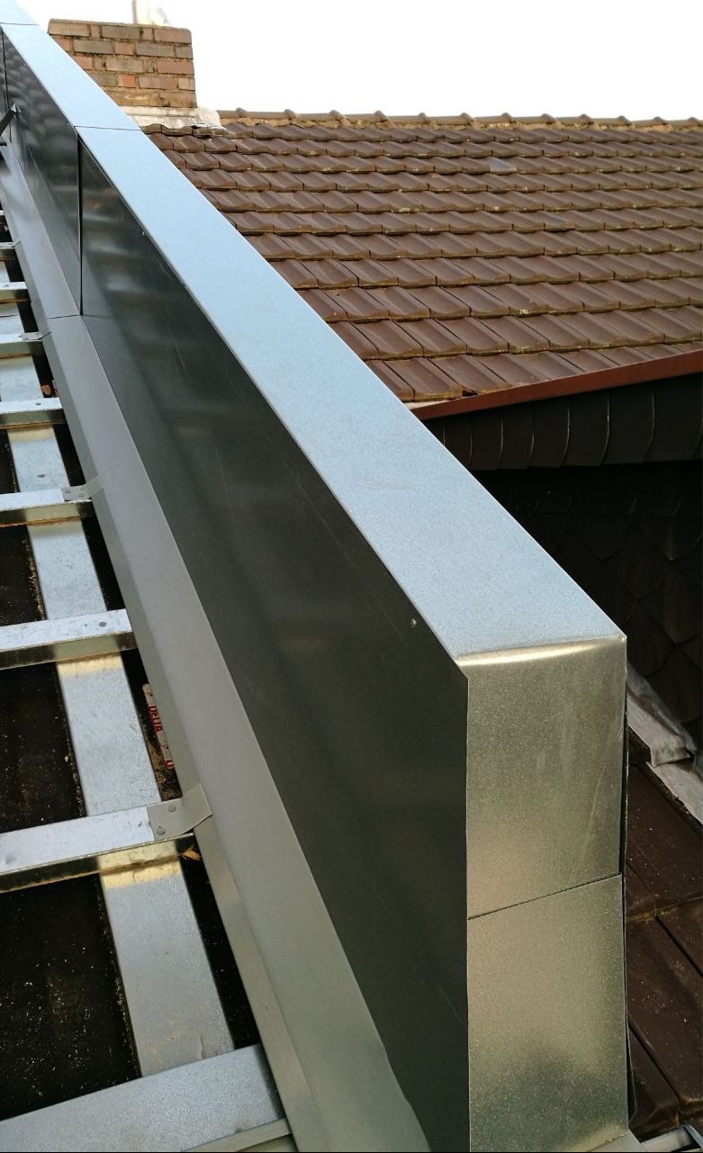 Szczegółowe ujęcie nowej, metalowej rynny dachowej, zamontowanej na brązowym dachu z dachówki ceramicznej. Widoczna konstrukcja wsporcza rynny i komin w tle.