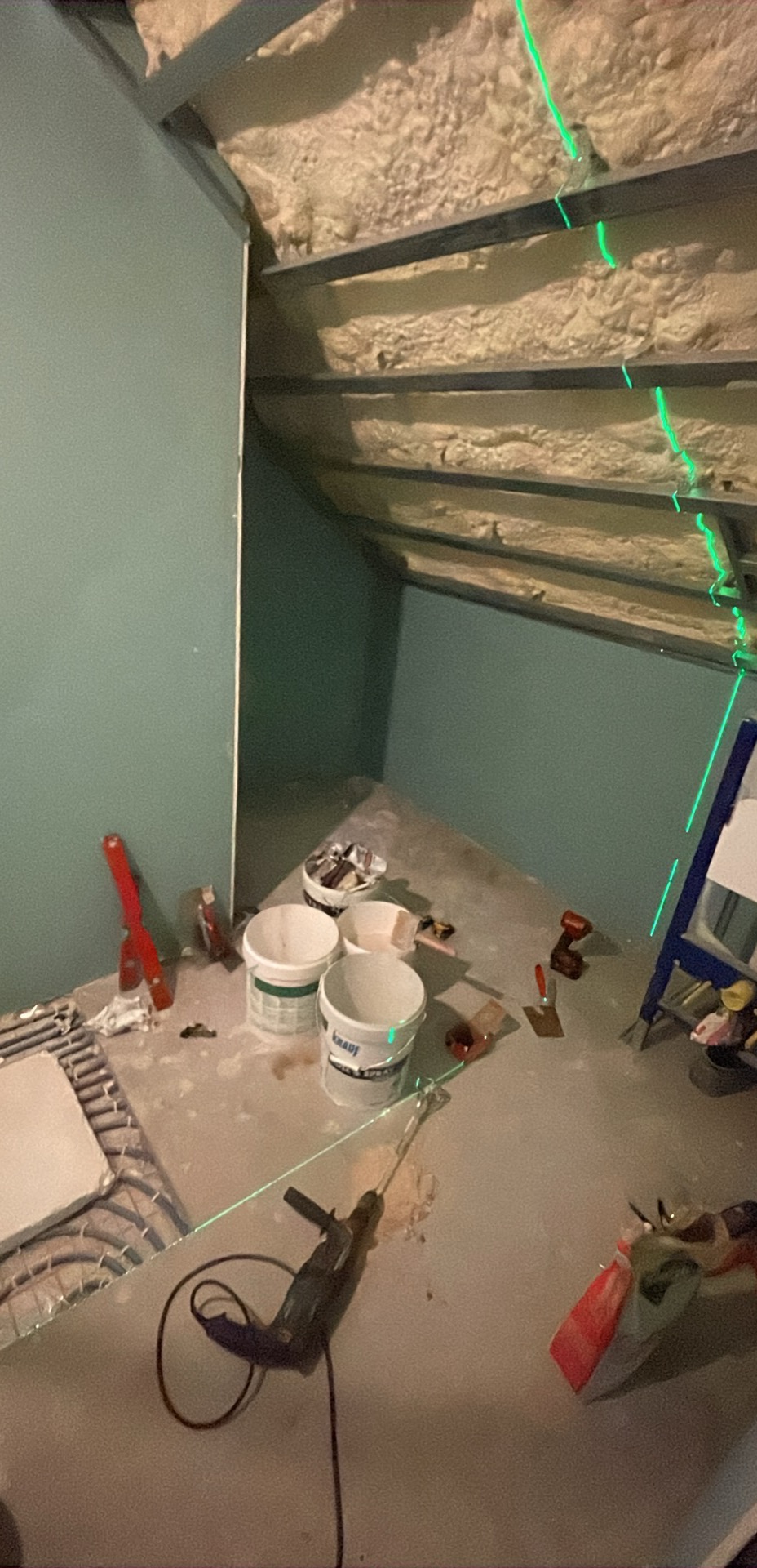 Poddasze w trakcie izolacji, widoczne profile, wełna mineralna, narzędzia i poziomica laserowa. Prace wykończeniowe na poddaszu.