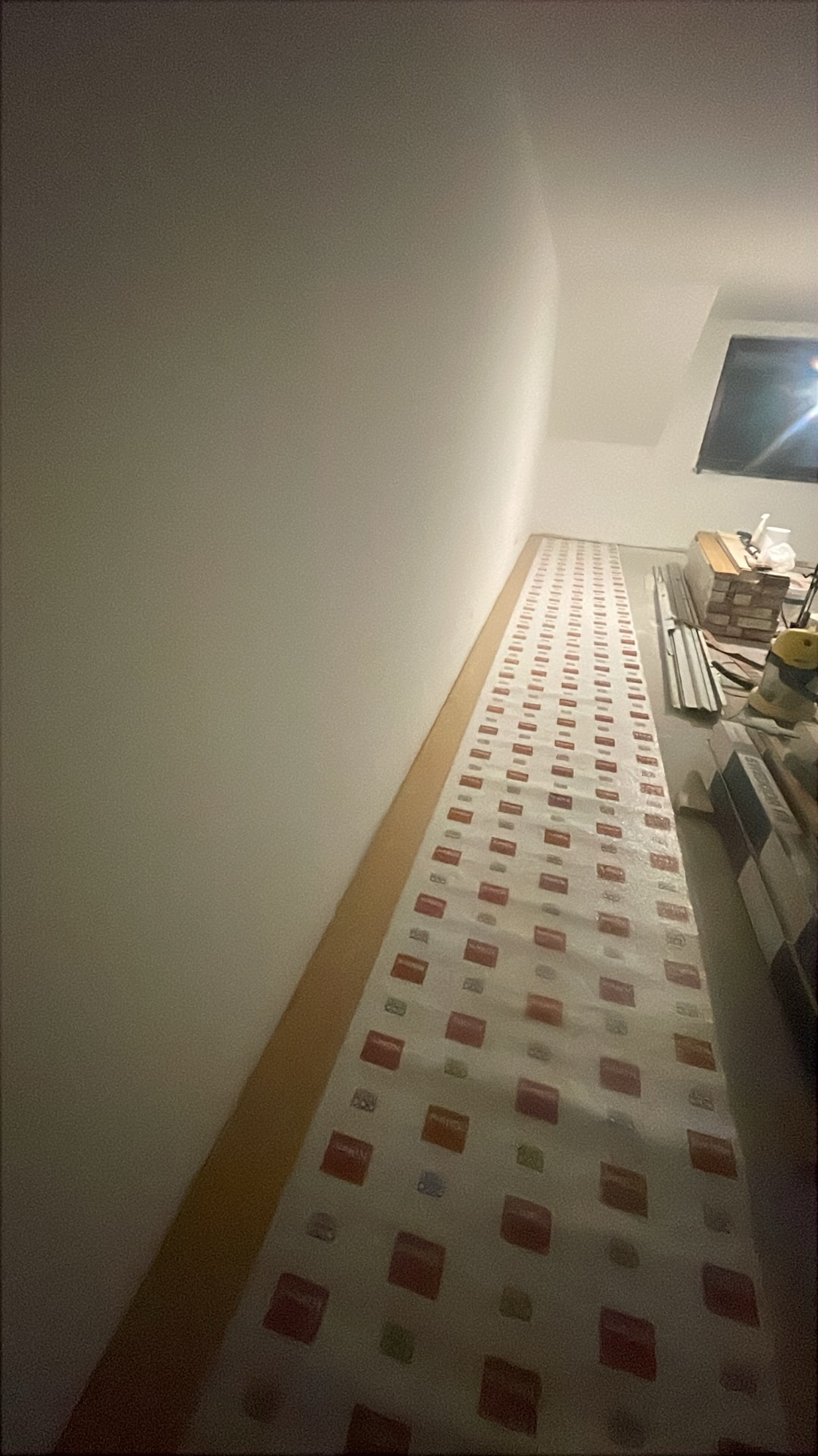 Przygotowanie do układania paneli: folia ochronna rozłożona na podłodze wzdłuż ściany, widoczne materiały i narzędzia w tle. Jasne wnętrze w trakcie remontu.