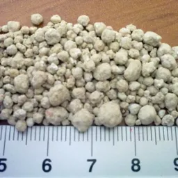 Beżowe granulki nawozu mineralnego, widoczne na tle drewnianej powierzchni z umieszczoną miarką w centymetrach.
