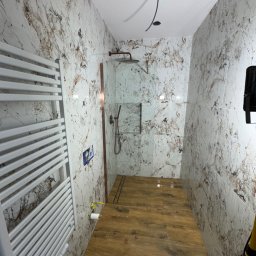 Przemysław Kieliński Remonty i Wykończenia - Nowoczesna łazienka z marmurowymi płytkami ściennymi i drewnopodobną podłogą. Widoczny grzejnik drabinkowy i kabina prysznicowa z deszczownicą. Minimalistyczny design.