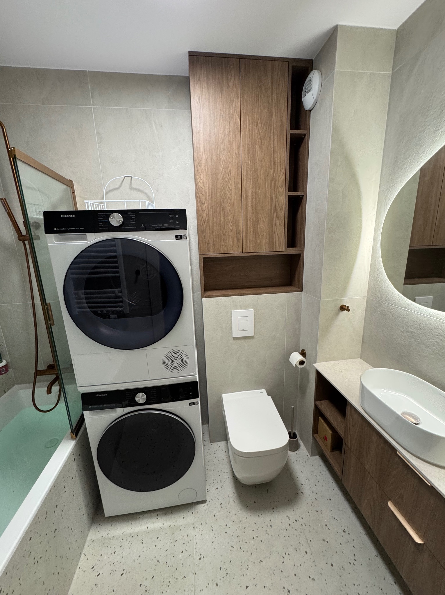 Nowoczesna łazienka z pralko-suszarką Hisense, umywalką nablatową i drewnianymi szafkami. Jasne płytki i oświetlenie LED tworzą minimalistyczny, funkcjonalny design.