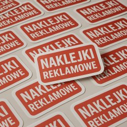 Flygraf - Czerwone, prostokątne naklejki reklamowe z zaokrąglonymi rogami, ułożone blisko siebie na jasnym tle. Widoczne napisy 'NAKLEJKI REKLAMOWE' w kolorze białym.