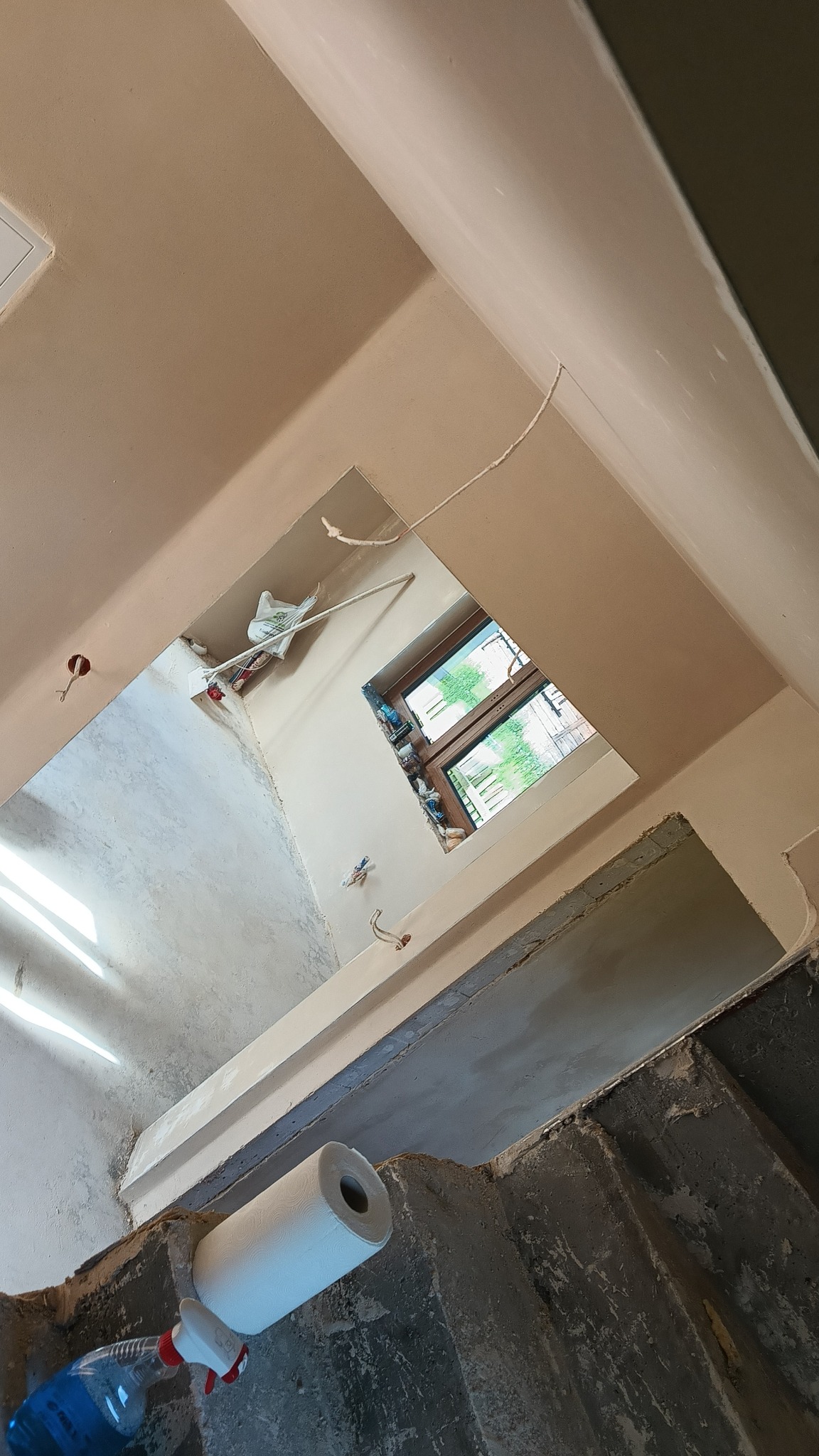 Świeżo położone tynki maszynowe na ścianach i suficie w pomieszczeniu z oknem. Widoczne narzędzia i materiały budowlane. Ujęcie z dołu, podkreślające gładkość powierzchni.