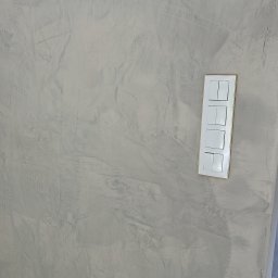 Sebastian Chmielewski - Ściana po szpachlowaniu z widoczną fakturą i zamontowanym panelem włączników światła z delikatną, złotą ramką. Widoczny fragment instalacji elektrycznej.