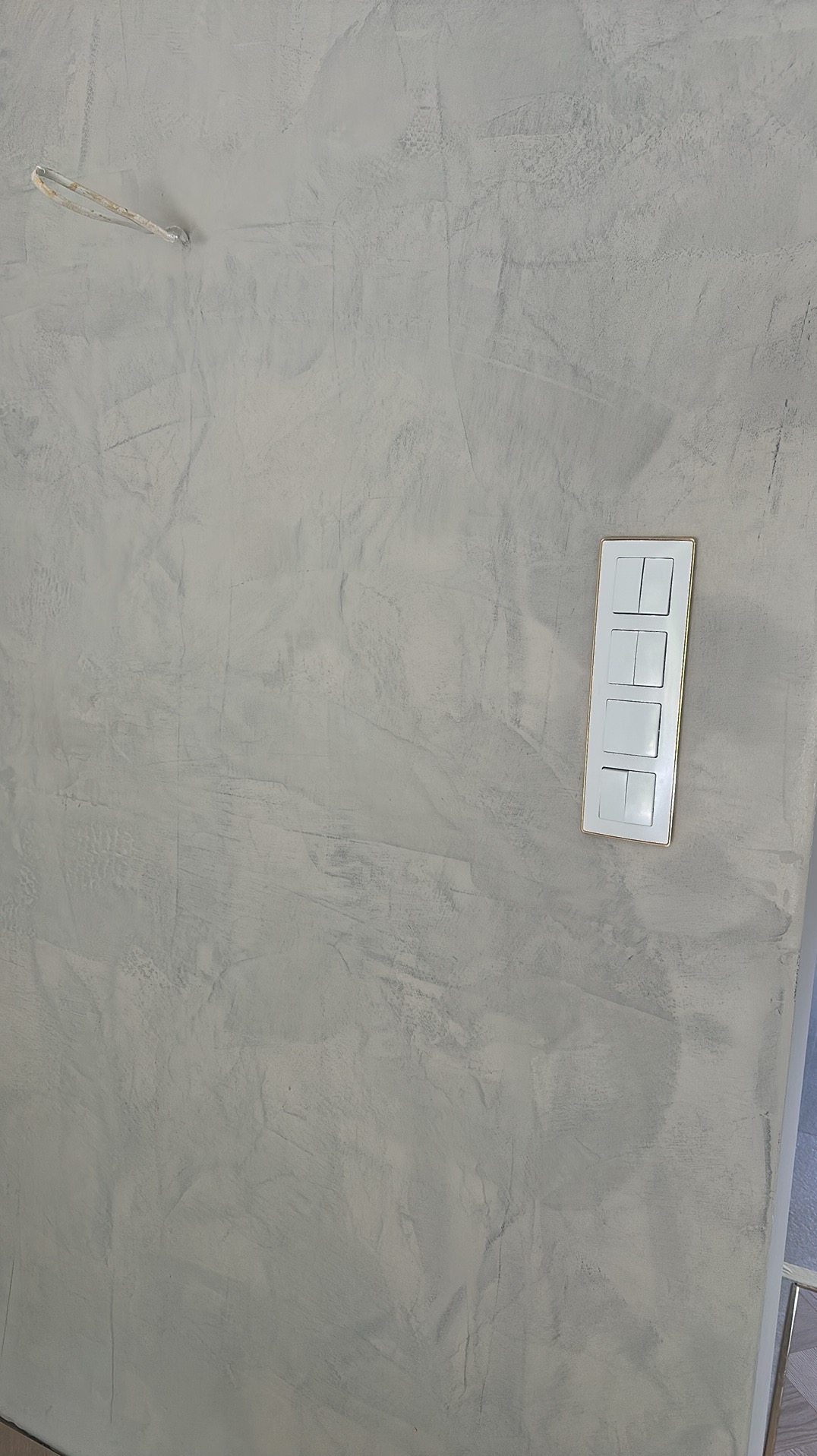 Ściana po szpachlowaniu z widoczną fakturą i zamontowanym panelem włączników światła z delikatną, złotą ramką. Widoczny fragment instalacji elektrycznej.