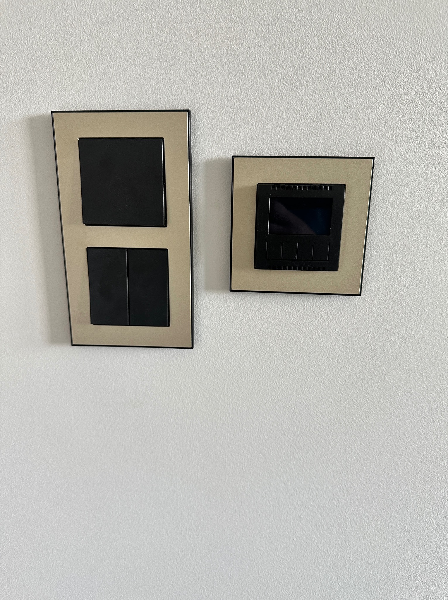Dwa panele na białej ścianie: podwójny włącznik światła i panel sterowania, oba w beżowych ramkach. Minimalistyczny design, nowoczesne wykończenie.