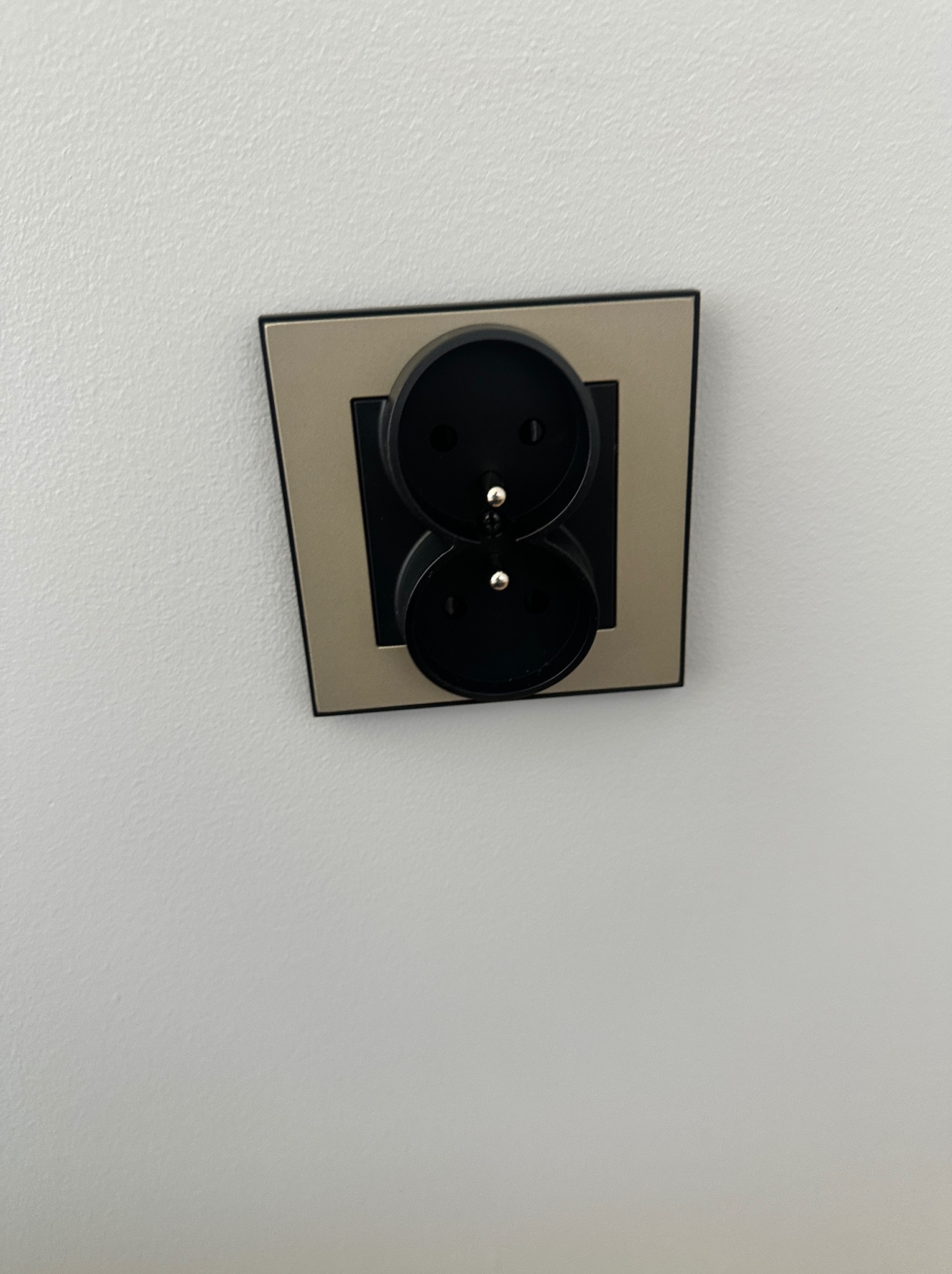 Podwójne gniazdko elektryczne w kolorze czarnym z beżową ramką, zamontowane na białej ścianie. Widok z dołu, ukazujący detale wykończenia.
