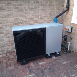 BLUETHERMX Adrian Pietrzyk - Pompa ciepła Daikin zamontowana na zewnątrz budynku w Lublinie, widoczna na tle ceglanej ściany i kostki brukowej. Instalacja z rurami i skrzynką sterowniczą.