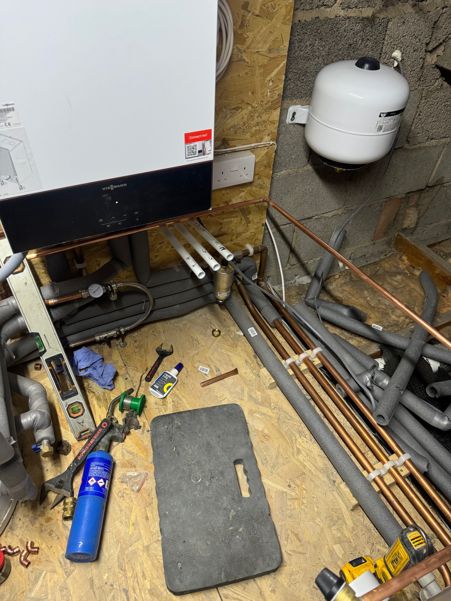 Montaż pieca gazowego Viessmann z widocznymi rurami miedzianymi, narzędziami i elementami instalacji w trakcie prac. Nieukończona instalacja w pomieszczeniu.
