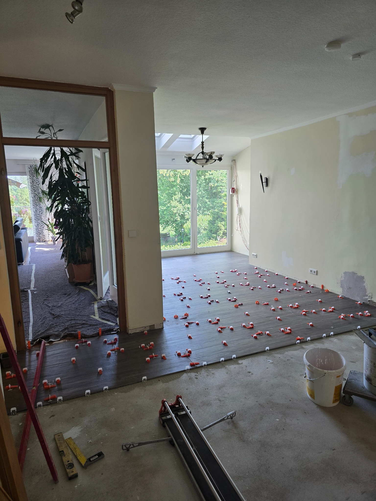 Układanie ciemnych płytek podłogowych z użyciem klipsów poziomujących. Widoczny fragment pomieszczenia z oknem i narzędzia glazurnicze.