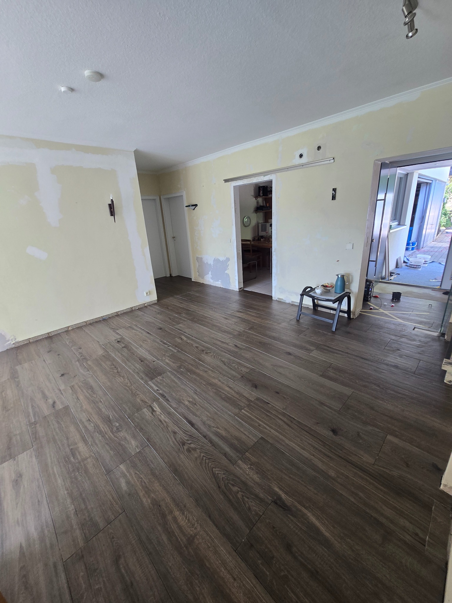 Ułożona podłoga z paneli imitujących drewno w jasnym pokoju z przygotowanymi ścianami do malowania. Widoczne drzwi przesuwne i akcesoria do picia.