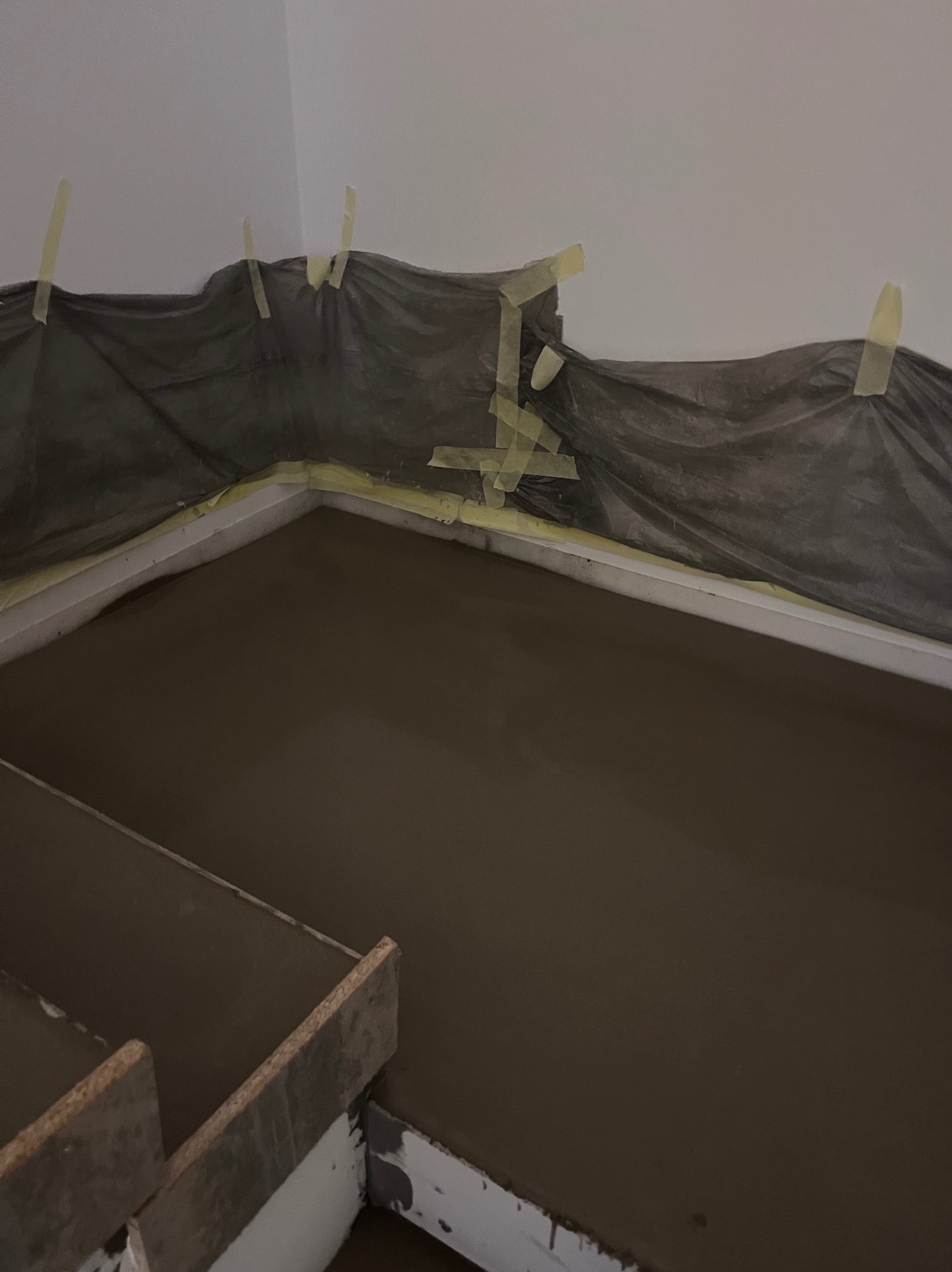 Świeżo wylana, gładka posadzka w trakcie prac wykończeniowych. Zabezpieczona folią i taśmą malarską przy ścianach. Widoczne elementy szalunku.