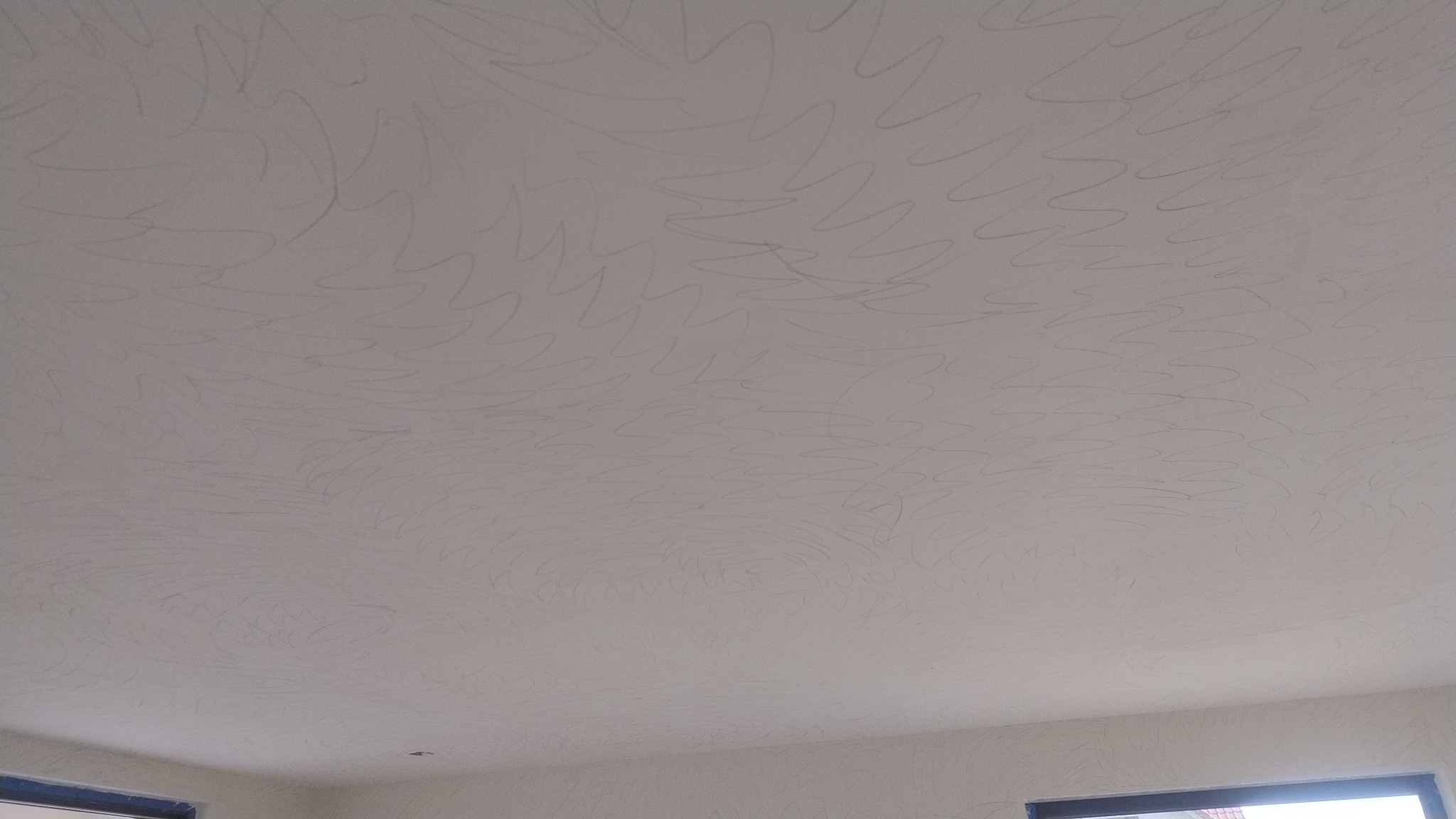 Biały sufit z delikatnym, nieregularnym wzorem przypominającym fale lub rysy, widoczny z perspektywy wnętrza, z fragmentami okien w dolnych rogach.
