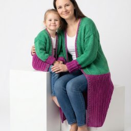 Krełowski Foto-Art - Uśmiechnięta mama obejmuje córkę, obie w dopasowanych, dzierganych, zielono-fioletowych kardiganach na białym tle. Sesja w jasnym, studyjnym oświetleniu.