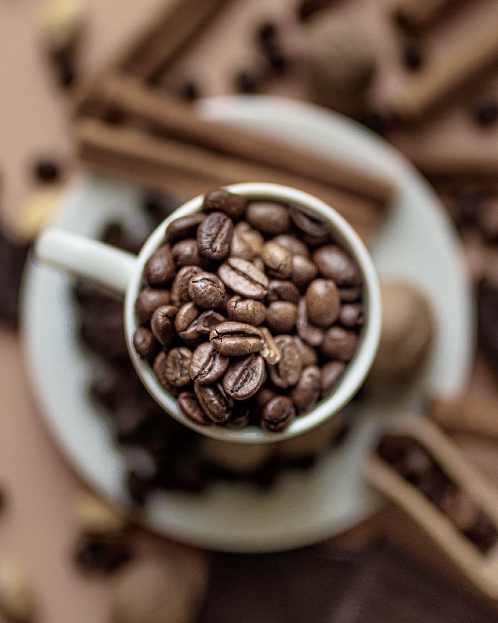 Aromatyczna kompozycja: filiżanka wypełniona ziarnami kawy na tle cynamonu, orzechów i ziaren kawy, uchwycona z góry w ciepłej tonacji brązów.