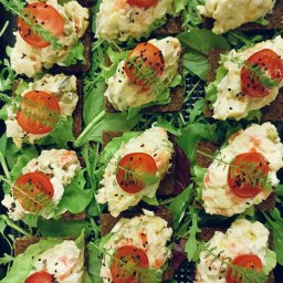 Red Target sp. z o o - Apetyczne kanapeczki na ciemnym pieczywie z sałatką jarzynową, pomidorkiem cherry i koperkiem, ułożone na świeżych liściach sałaty. Elegancka kompozycja kulinarna.