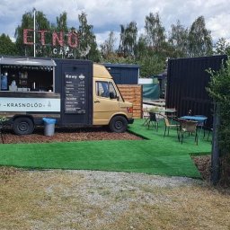 Red Target sp. z o o - Mobilna kawiarnia 'Krasnolód' w food trucku z menu kaw i cennikiem lodów, otoczona zielenią i stolikami na zewnątrz. Letnia atmosfera.