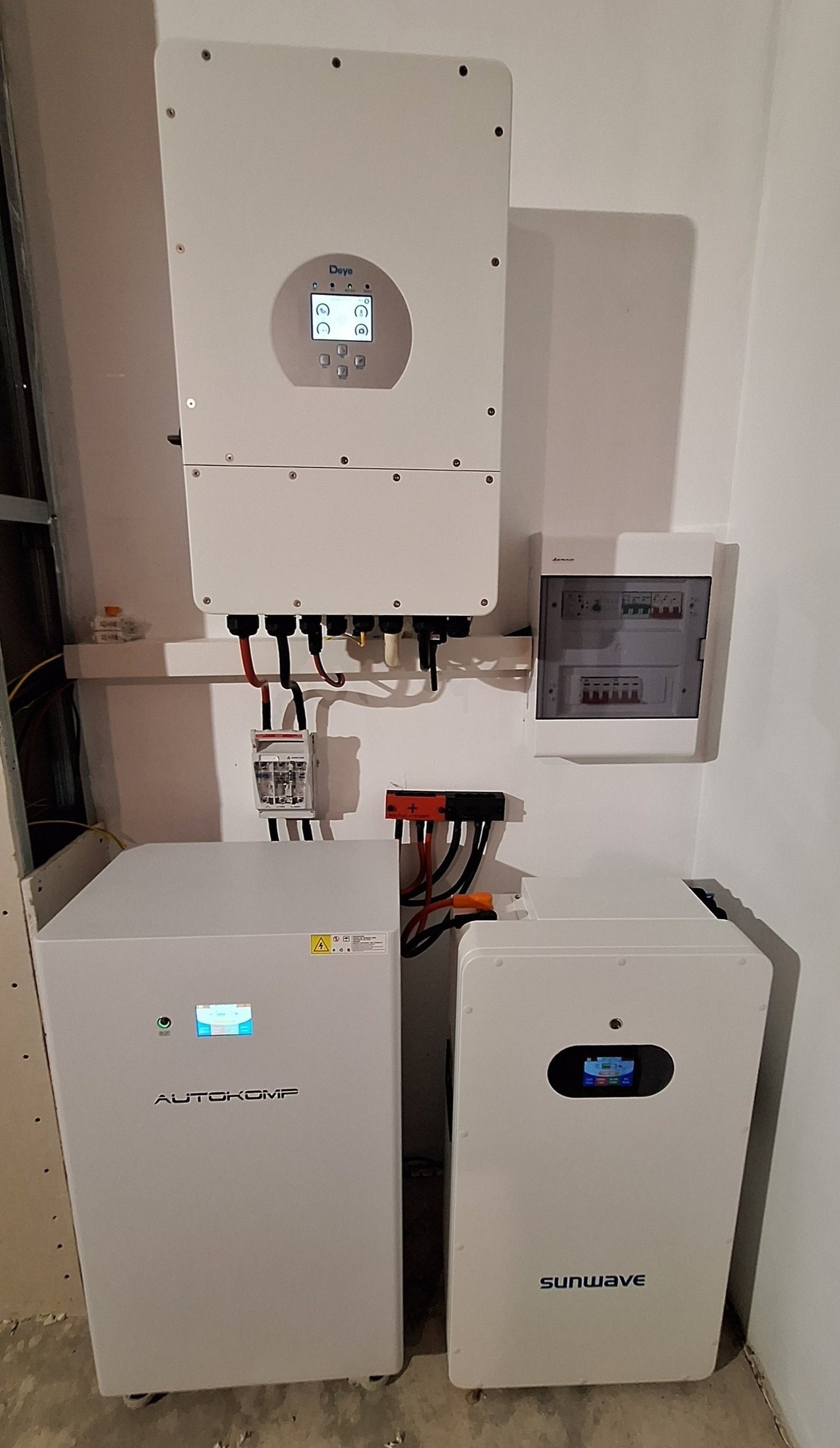 Kompletna instalacja fotowoltaiczna w pomieszczeniu: inwerter Deye, akumulatory Autokomp i Sunwave, zabezpieczenia. Widoczne kable i elementy montażowe.